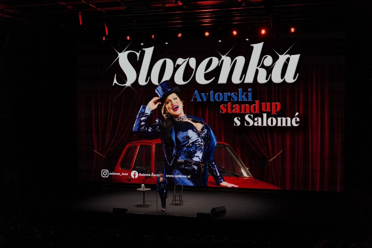 Salome na odru Odiseje pred veliko projekcijo plakata za predstavo Slovenka.